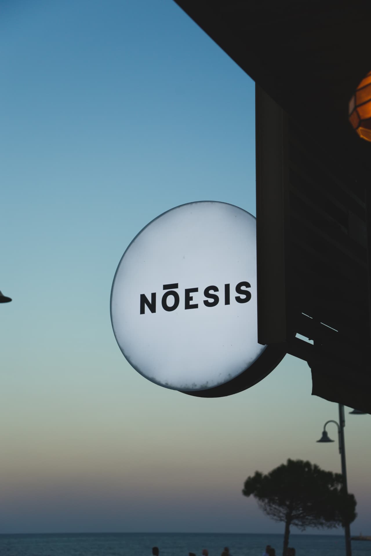The illuminated Nōesis sign above the sea at dusk