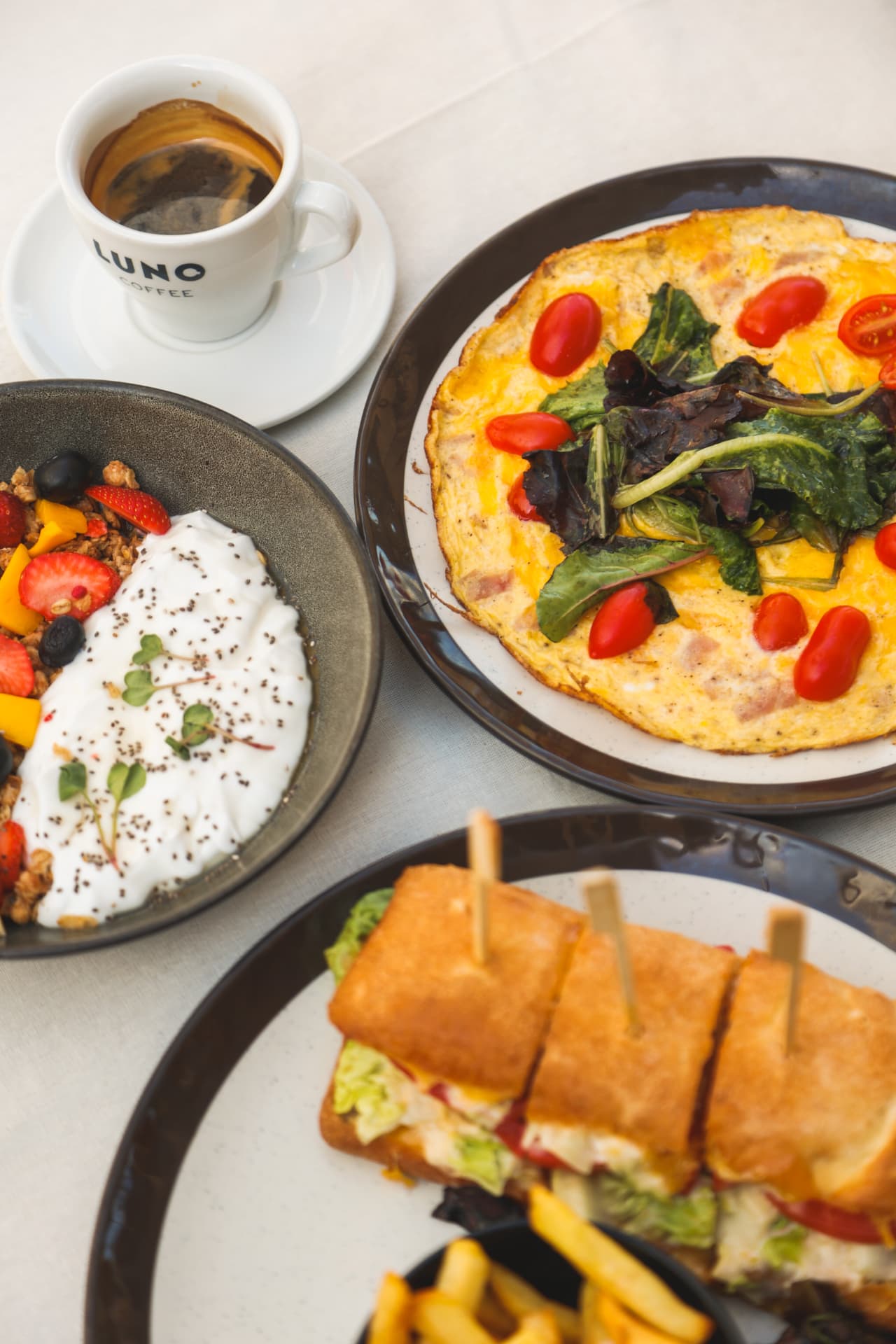 Brunch table with omelette, fruit bowl, sandwich and coffee at Nōesis
